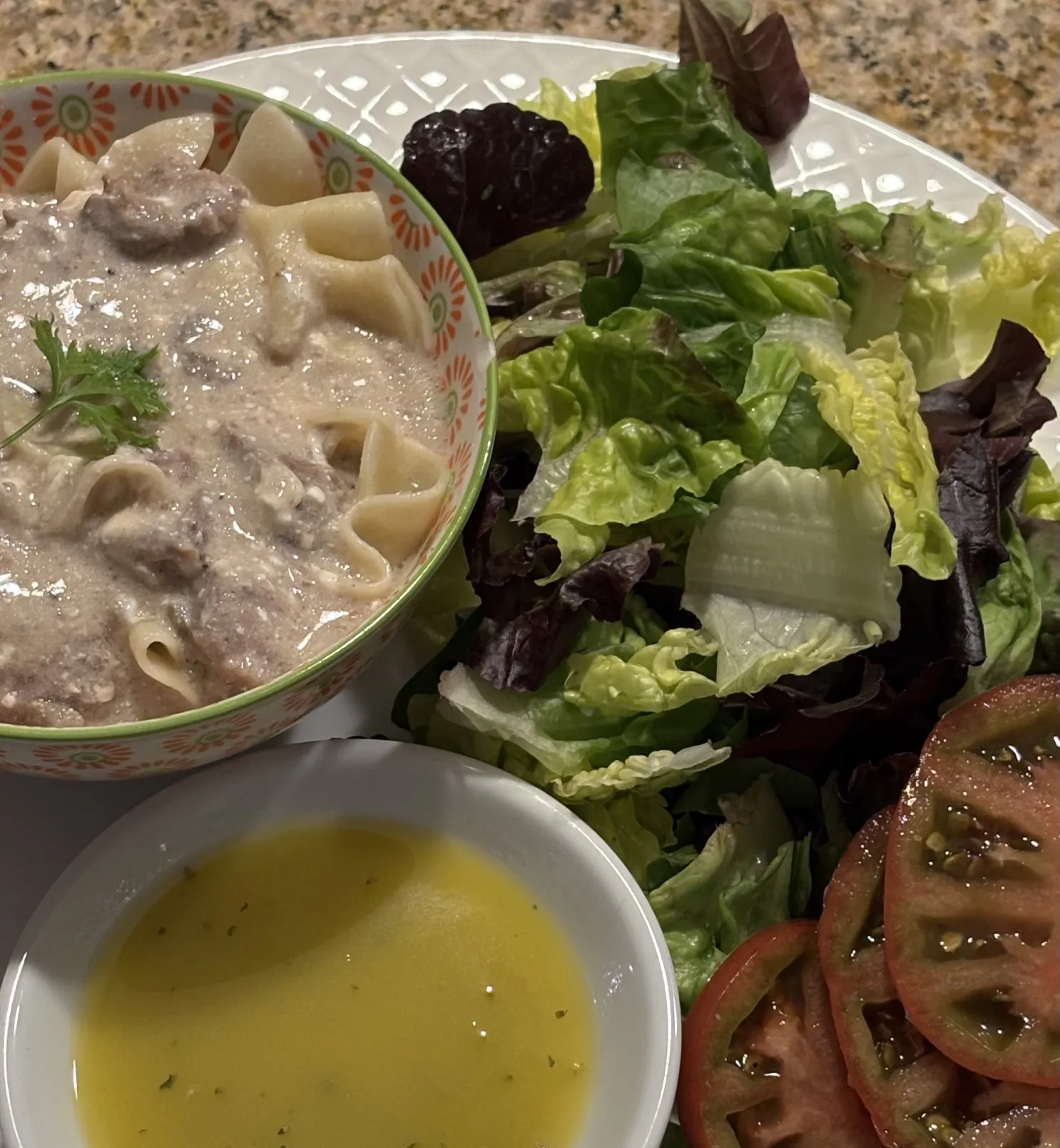 Bowl of creamy pasta, side salad with tomato slices, and a small dish of yellow dressing on a plate.